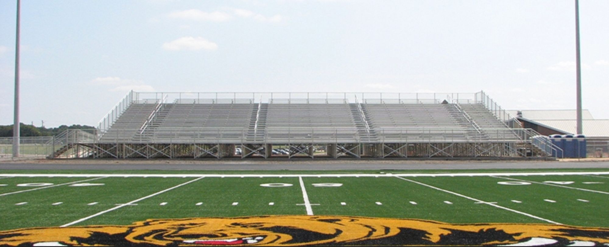 We see a photograph of a set of high school football bleachers, taken from the center of a field, which is within the bottom crop of the frame.